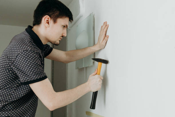 un giovane martella un tassello in un buco sul muro. - lifehack foto e immagini stock